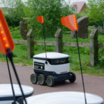 Starship robot travelling past row of robots on footpath